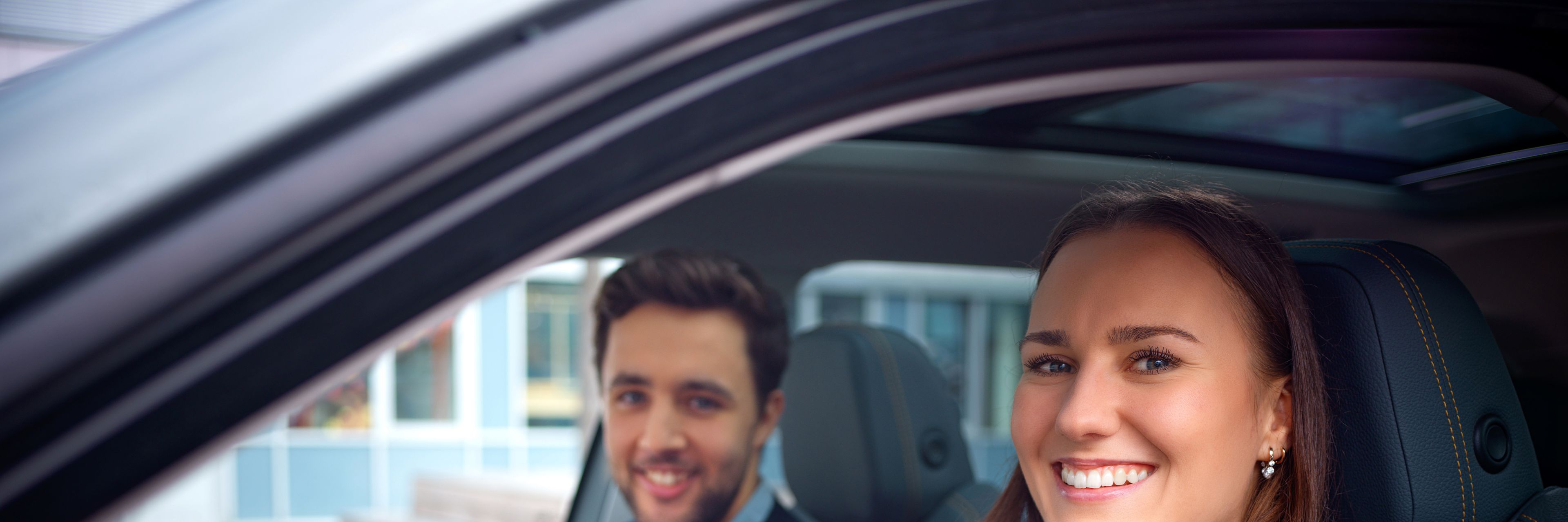 Two people sit in a car and smile.