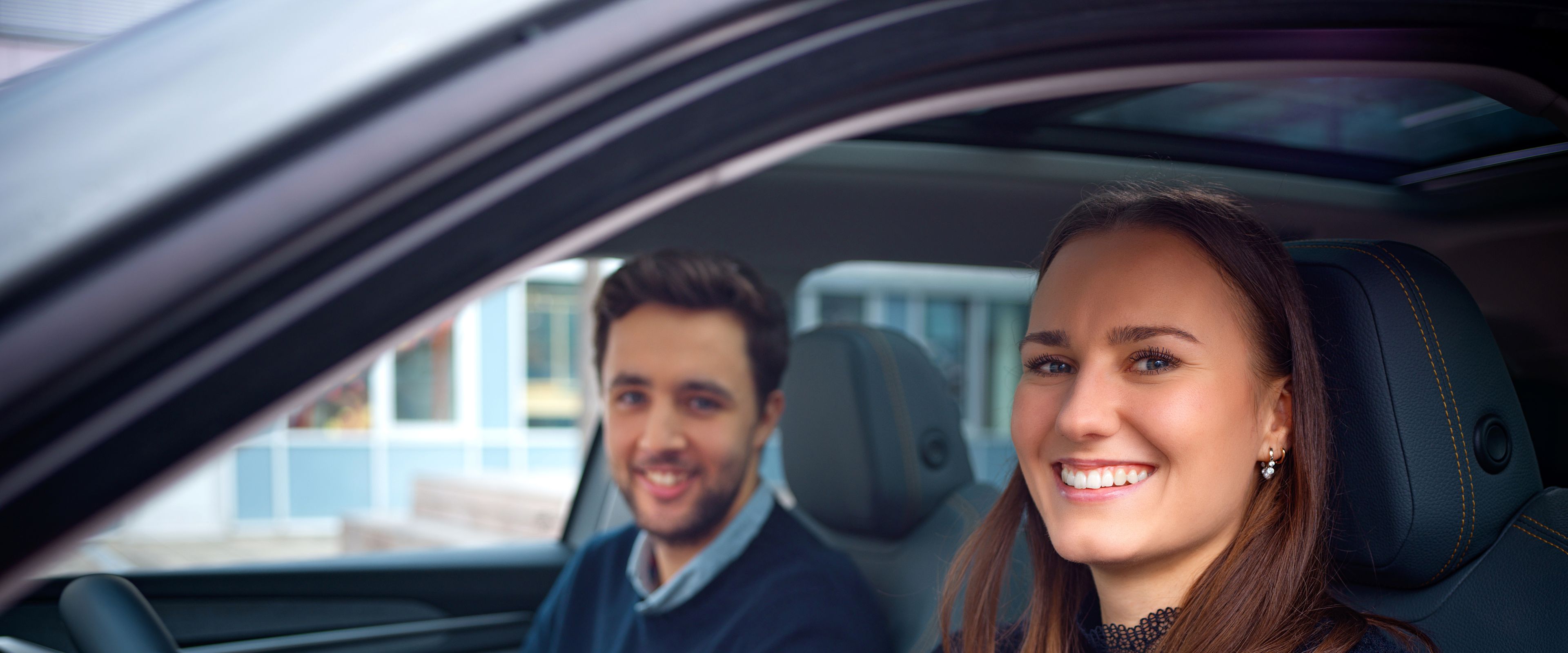 Two people sit in a car and smile.