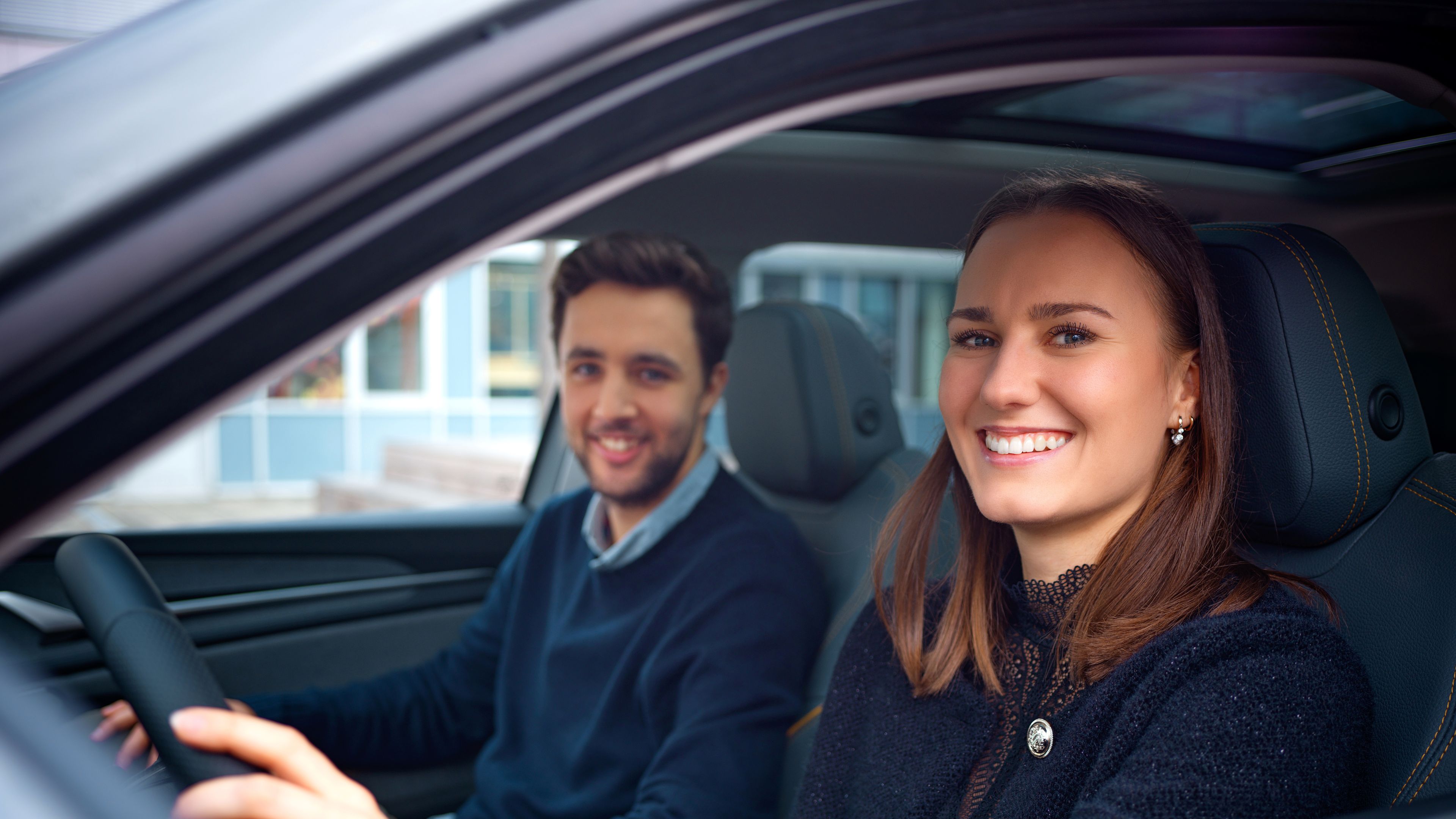 Two people sit in a car and smile.