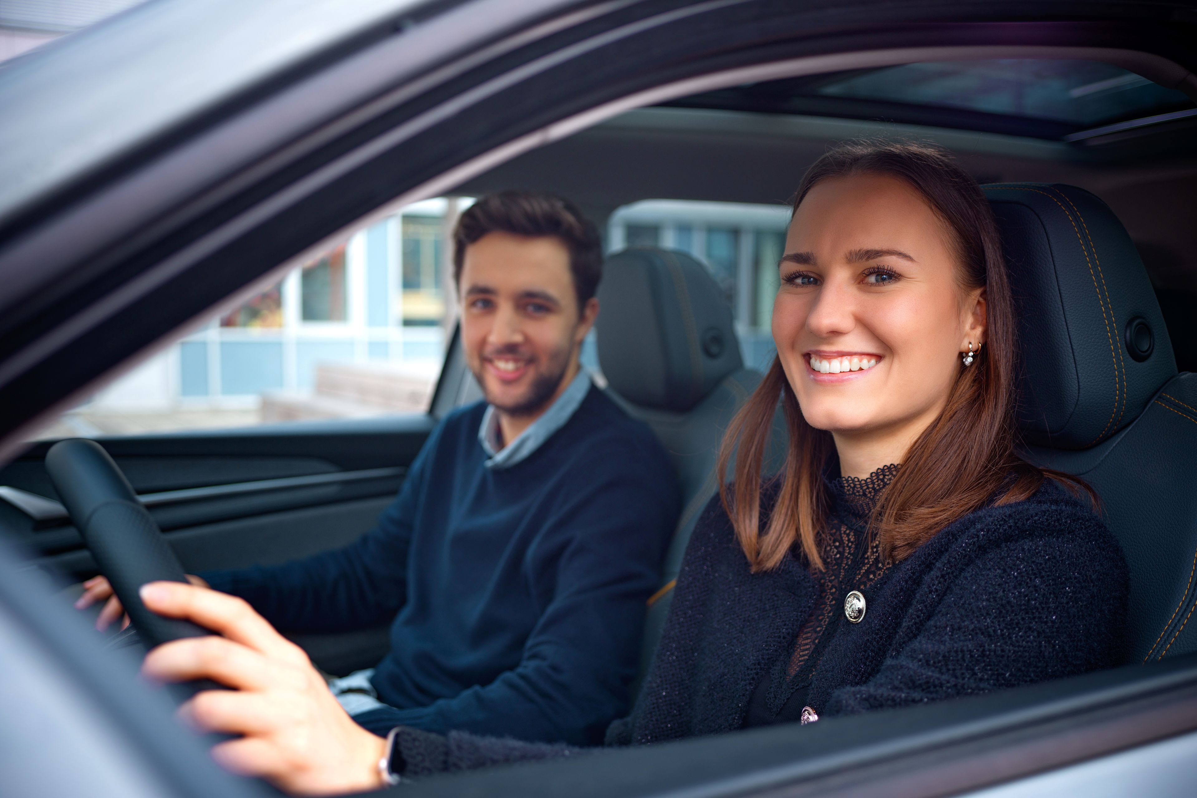 Two people sit in a car and smile.