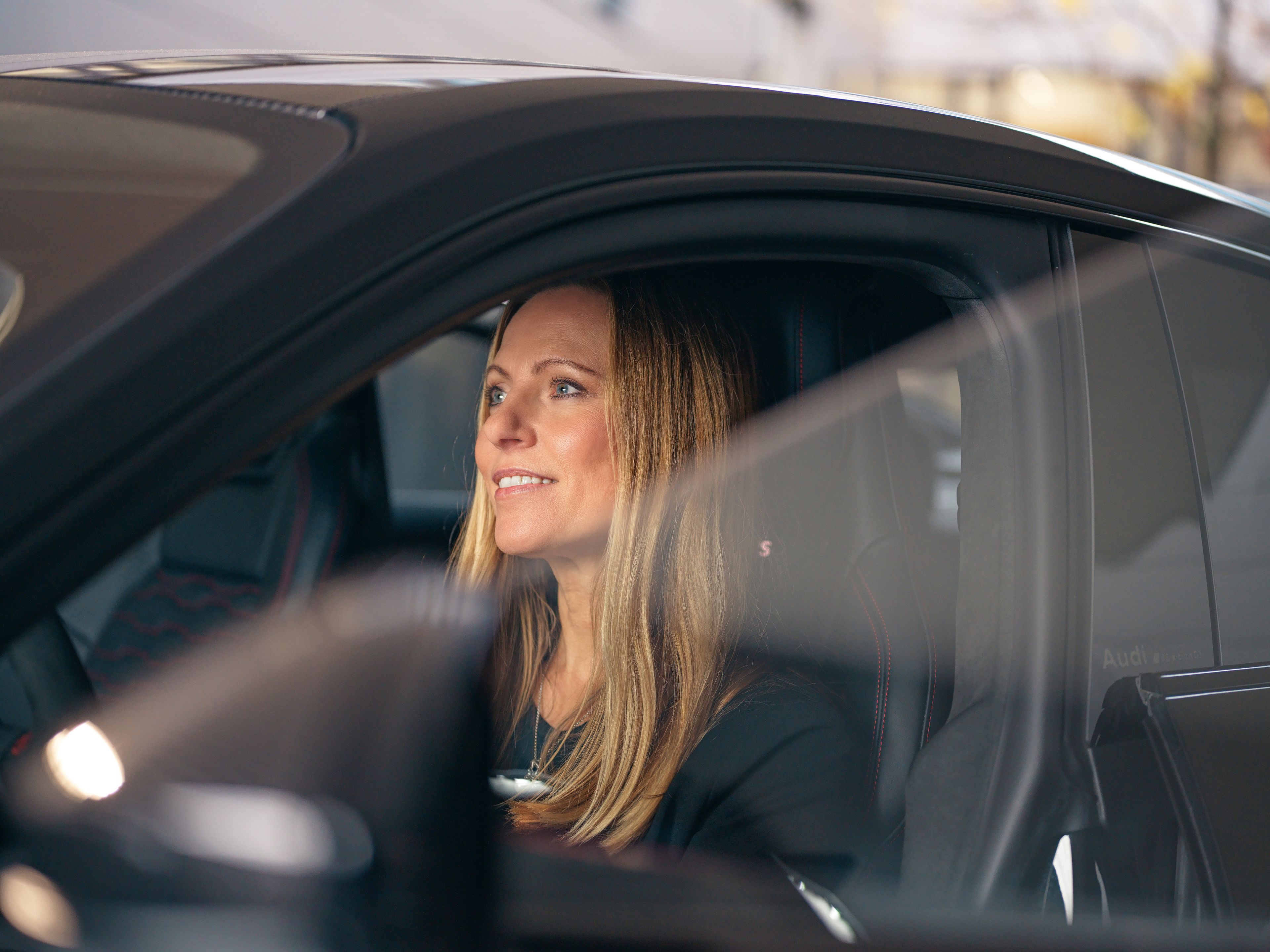 A lady is sitting in a black car.