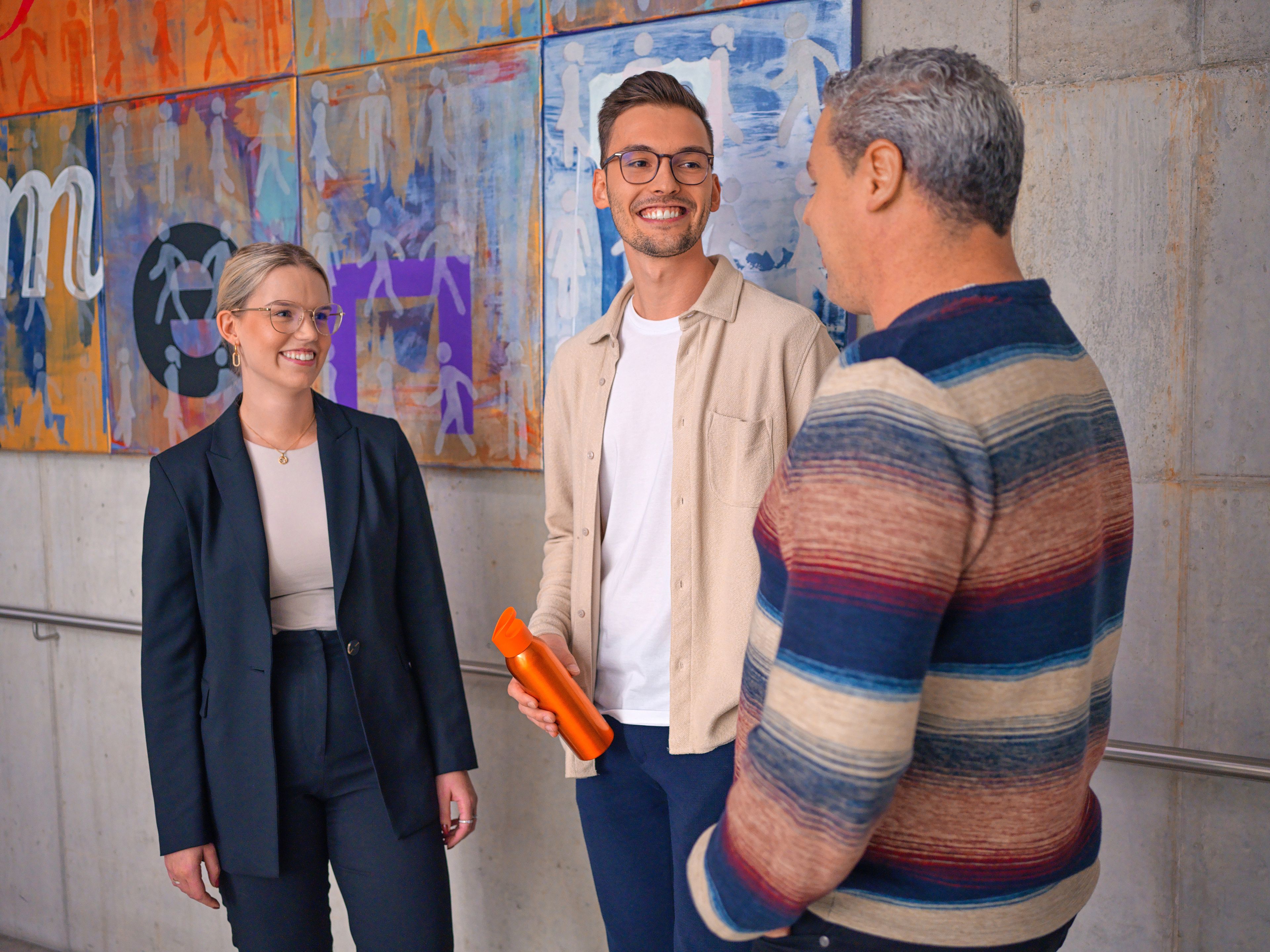 Hárman beszélgetnek egy lépcsőházban, mögöttük egy színes modern festmény.