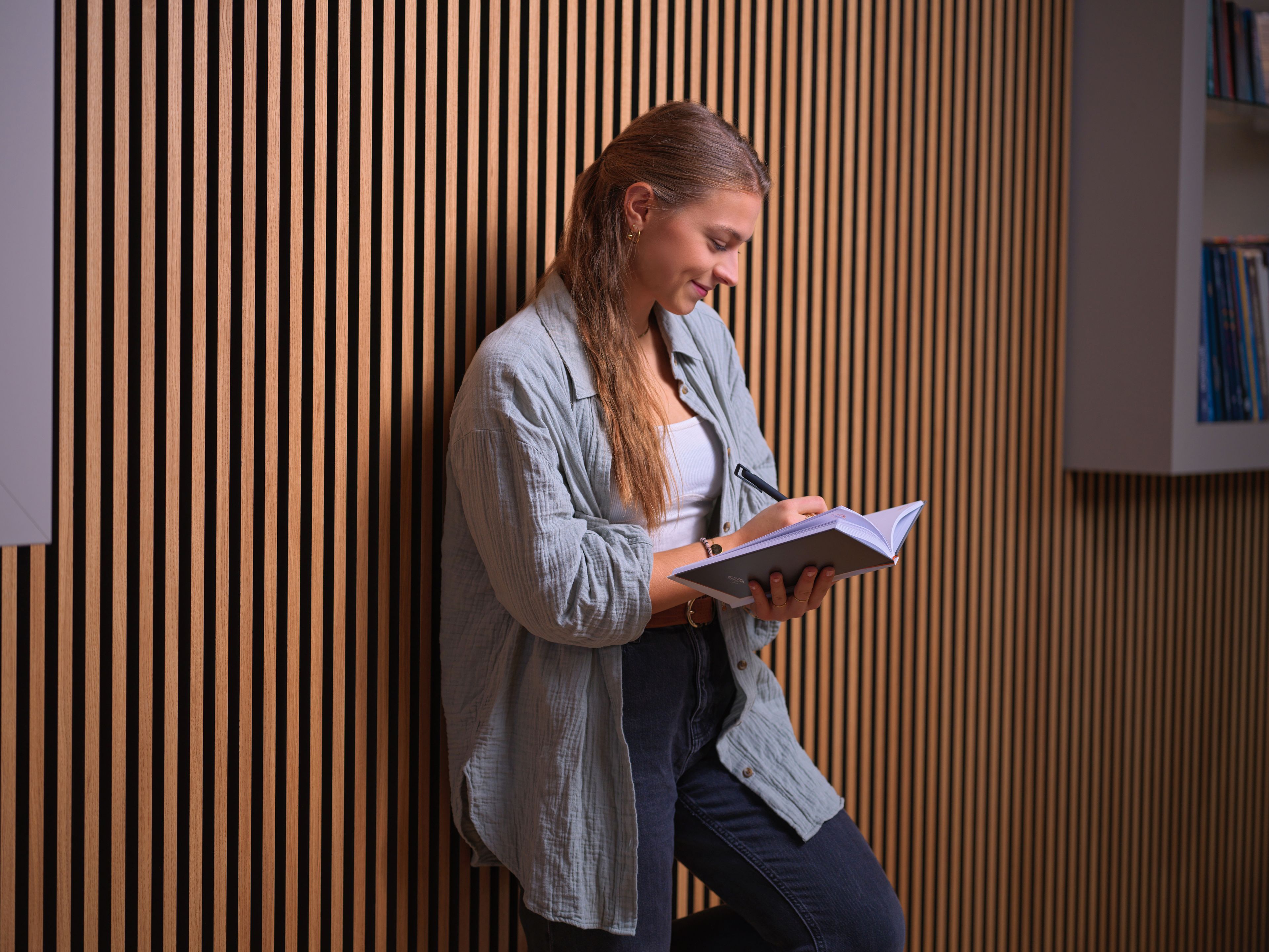 A young girl leans against the wall and takes notes in a notebook.