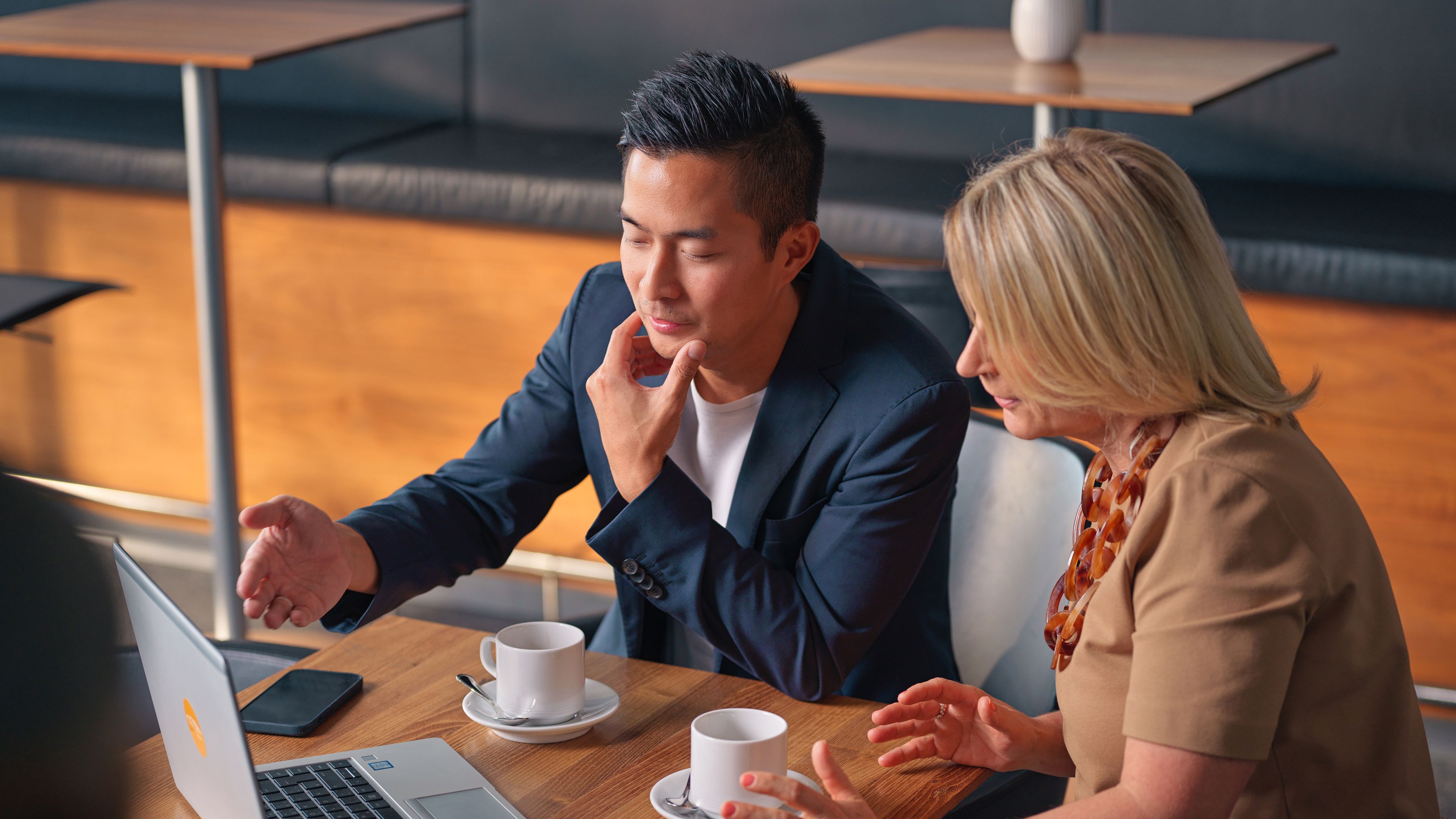 Two people sitting in a café, looking at a laptop