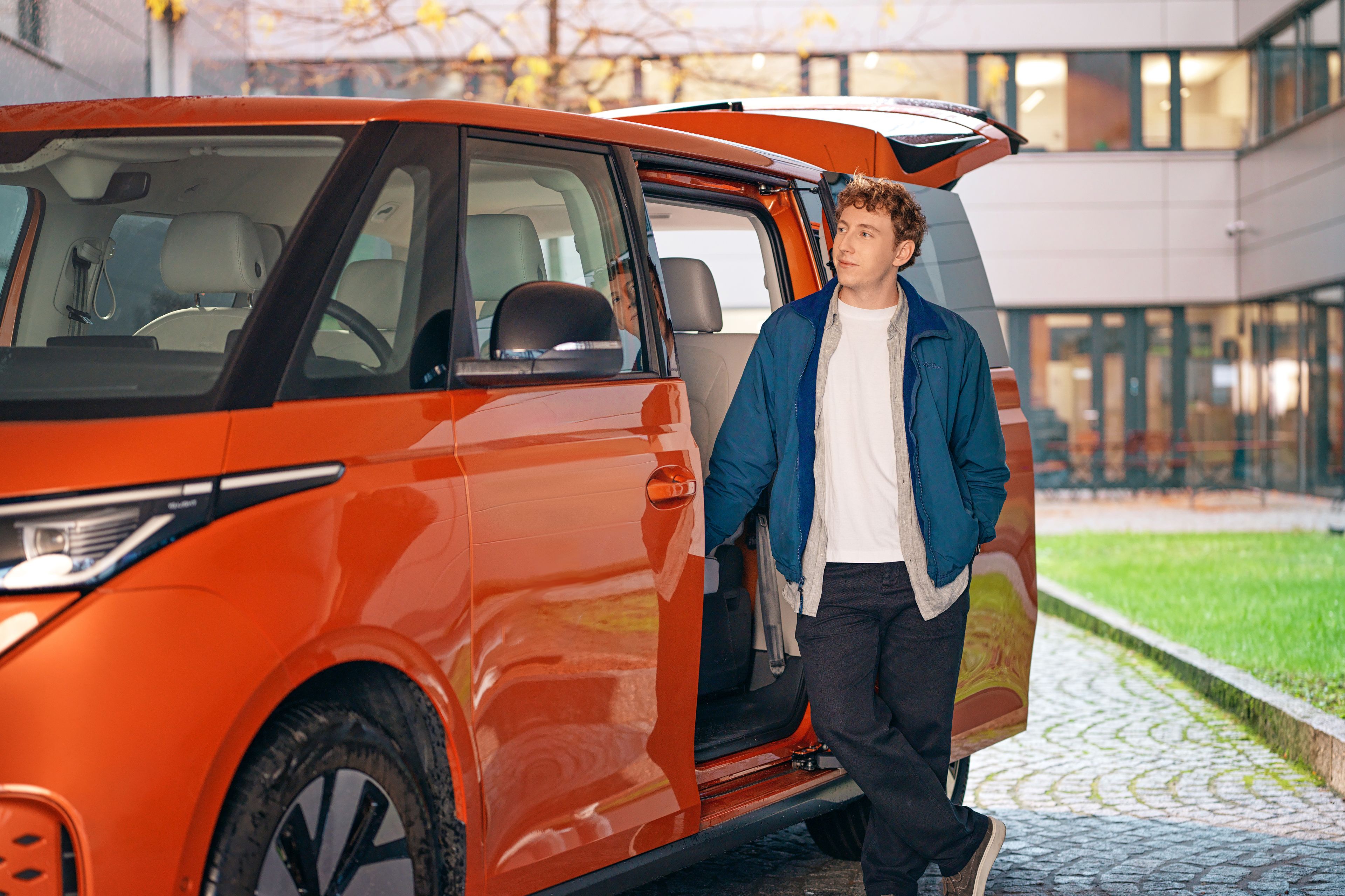A young man stands in the open door of an orange ID Buzz.