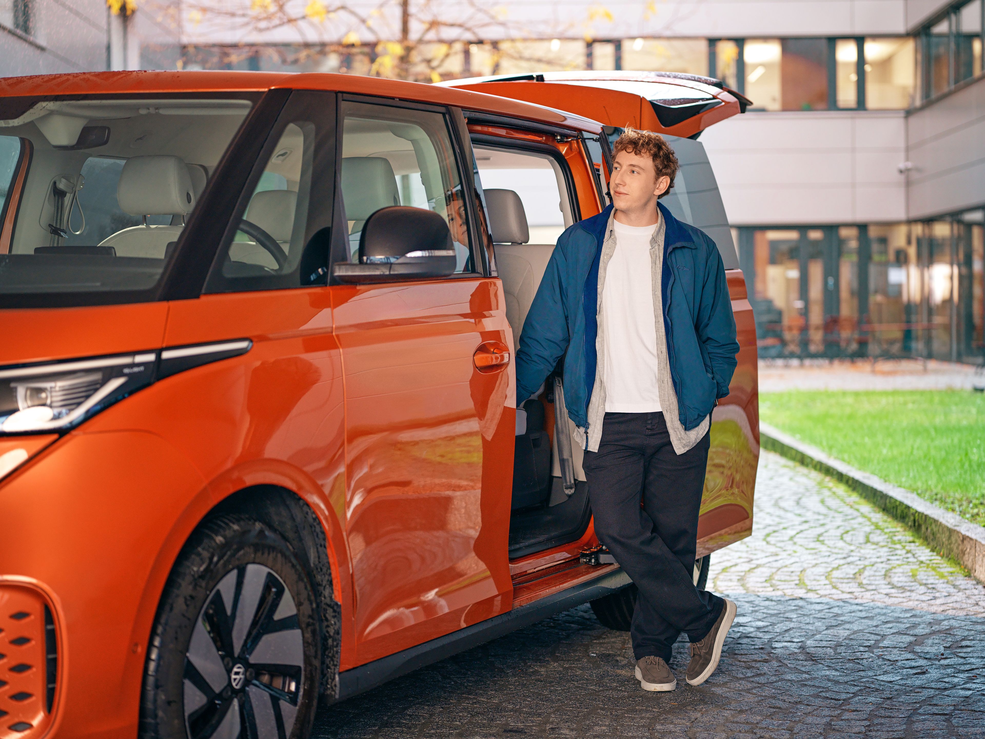 A young man stands in the open door of an orange ID Buzz.