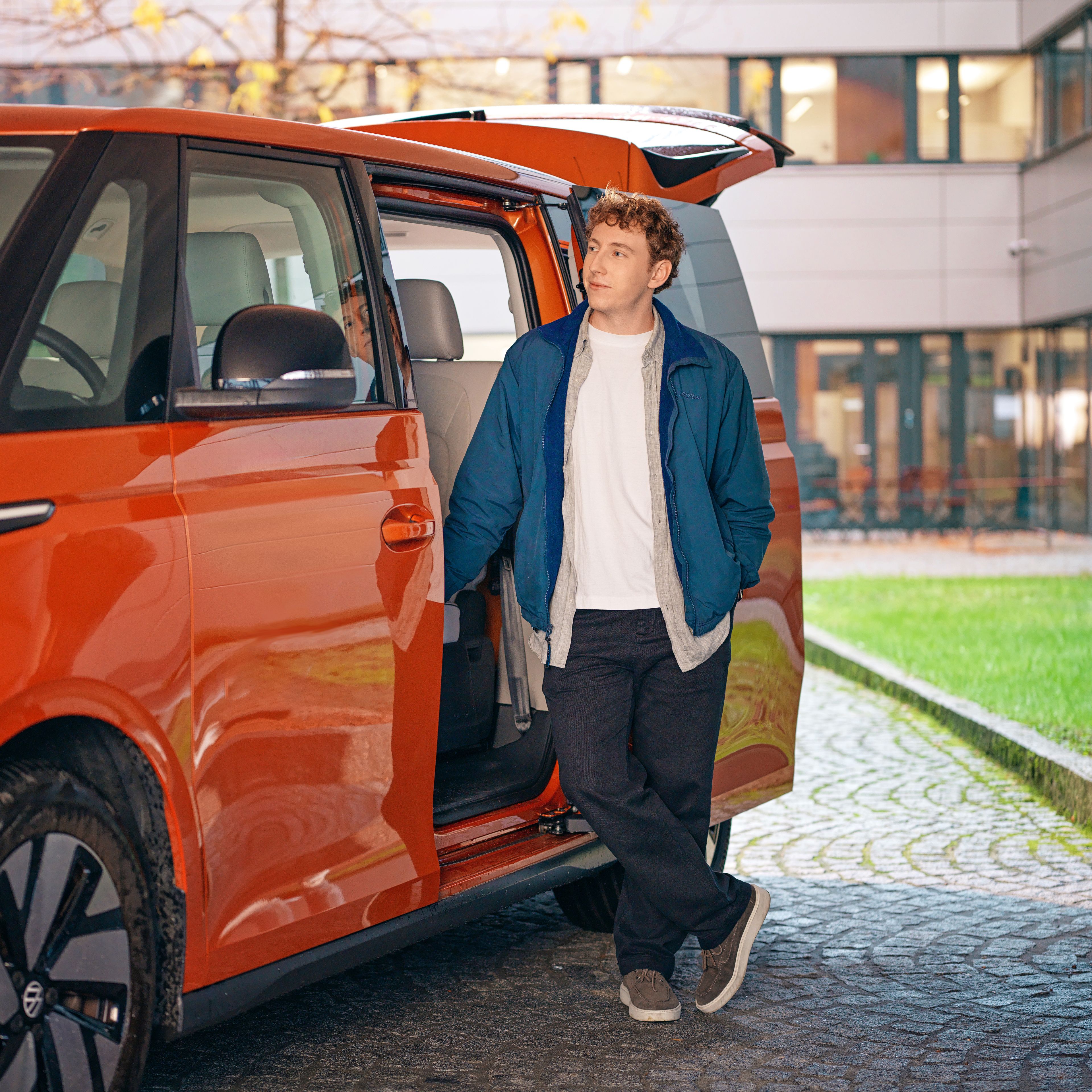 A young man stands in the open door of an orange ID Buzz.