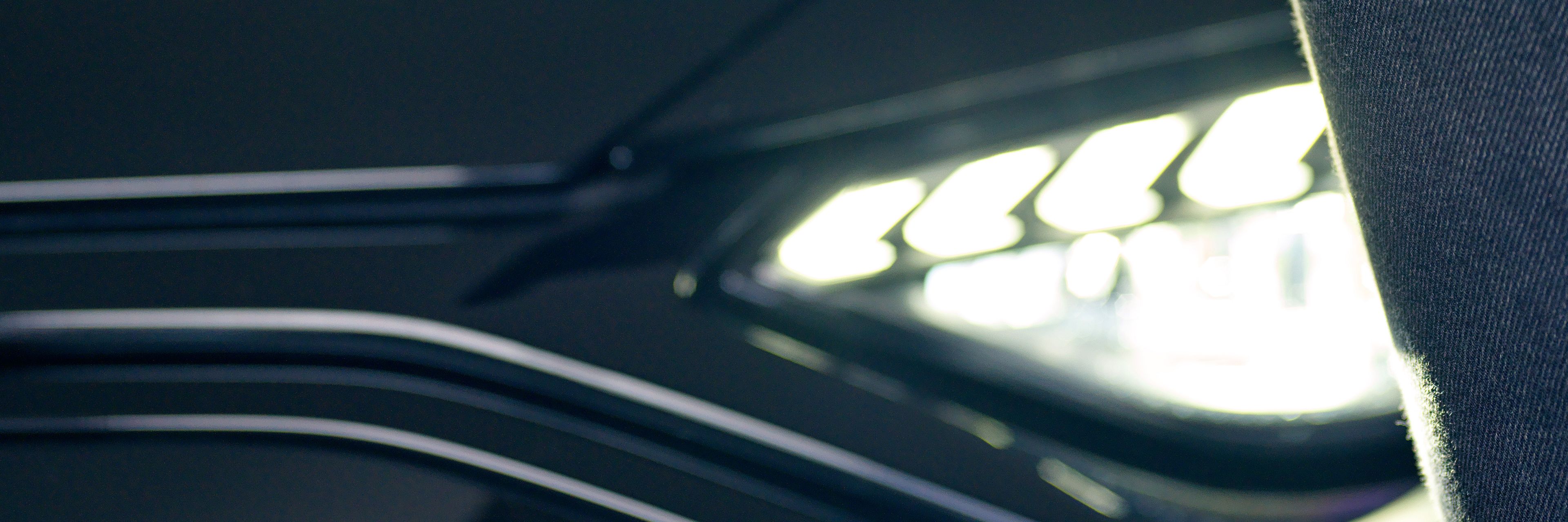 A car opener is in the hand of a lady, behind it you can see the headlight of a black car.