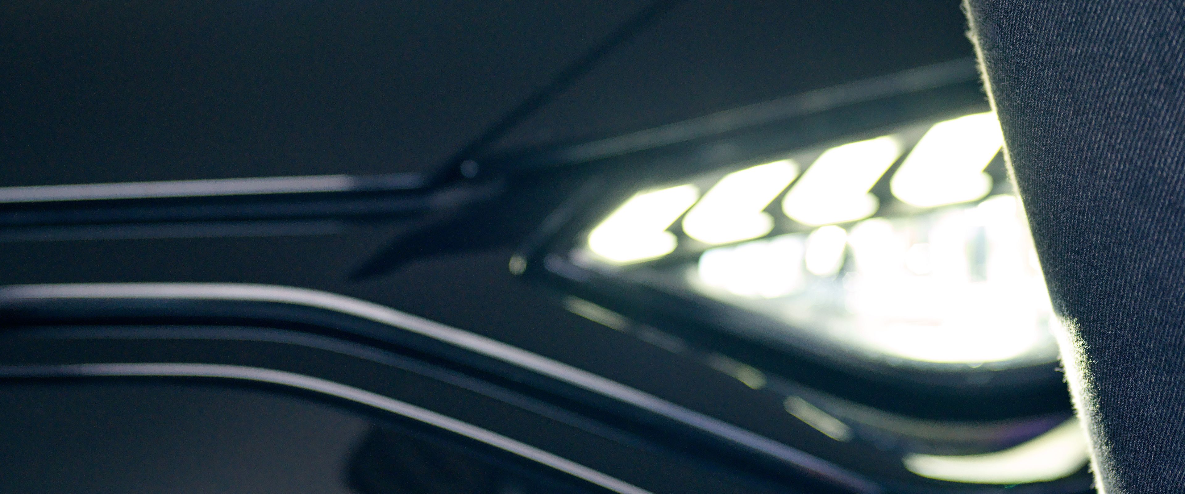 A car opener is in the hand of a lady, behind it you can see the headlight of a black car.