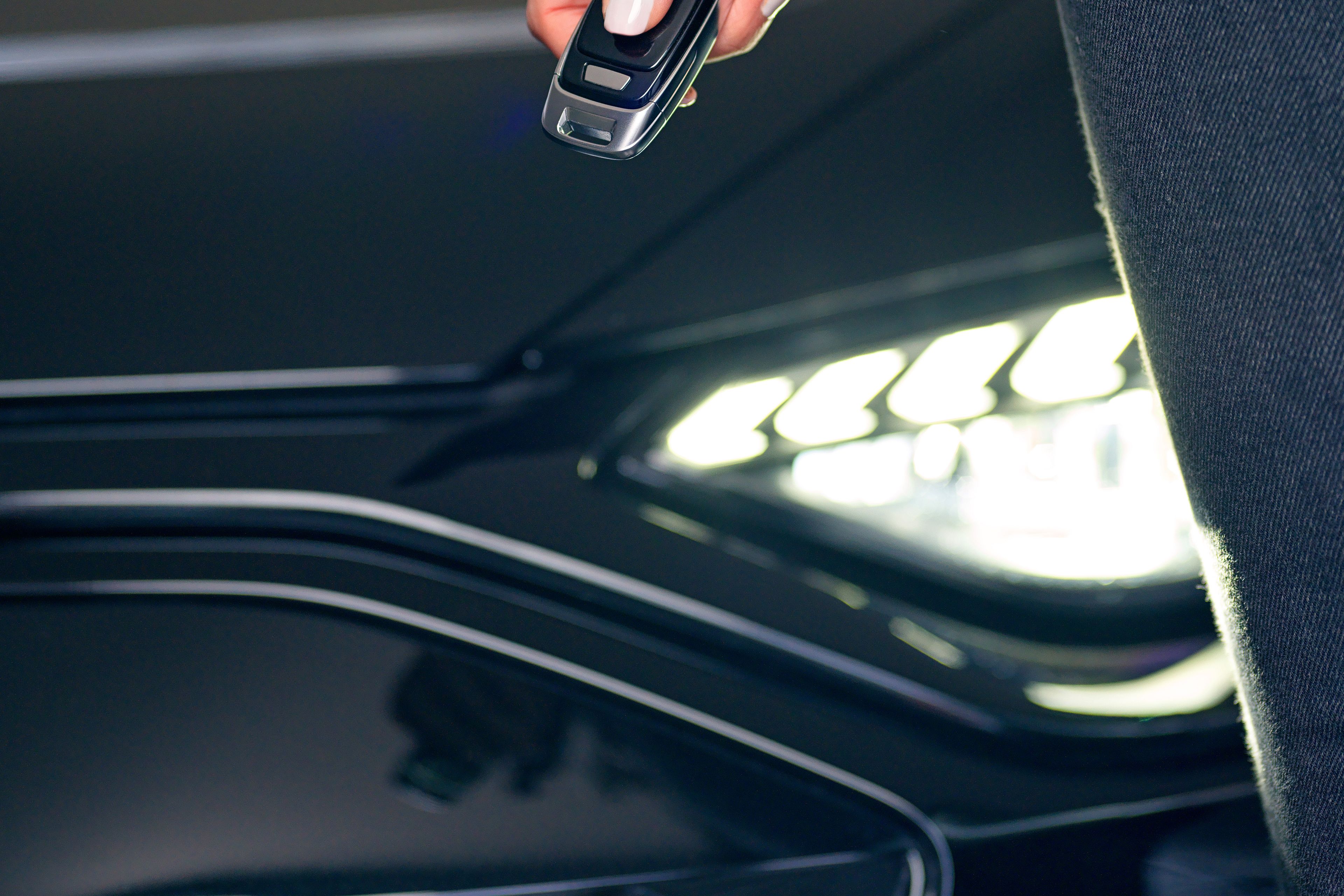 A car opener is in the hand of a lady, behind it you can see the headlight of a black car.