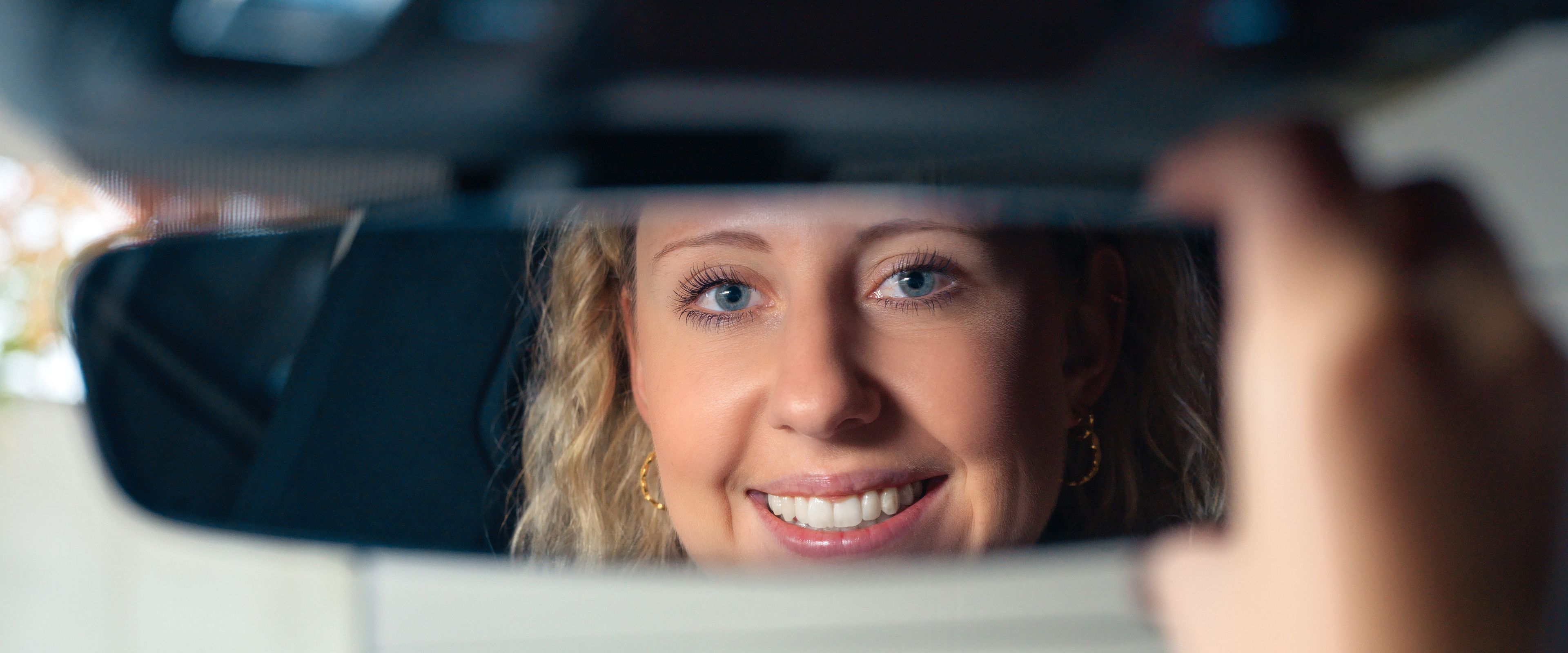 A lady adjusts a rearview mirror.