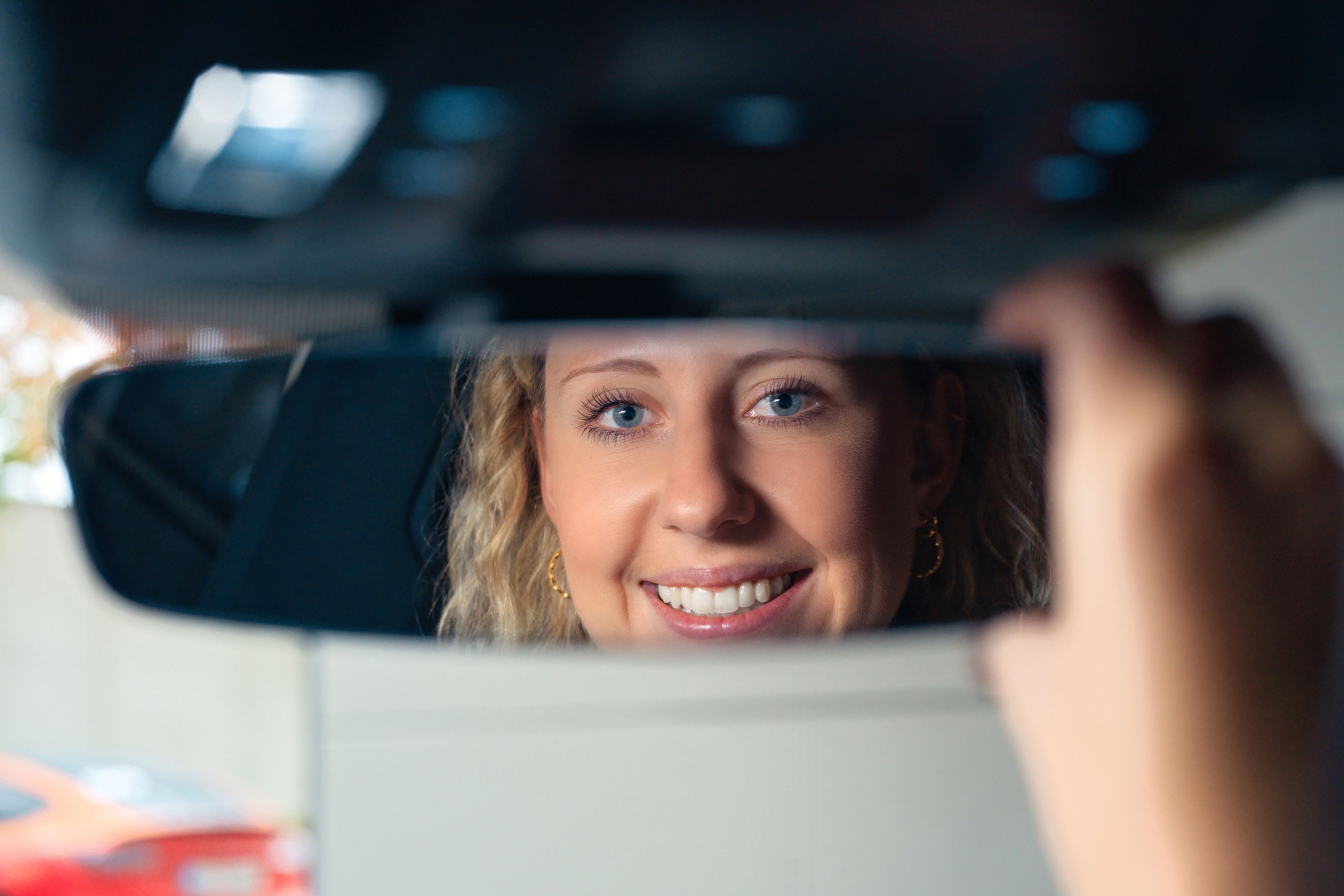 A lady adjusts a rearview mirror.