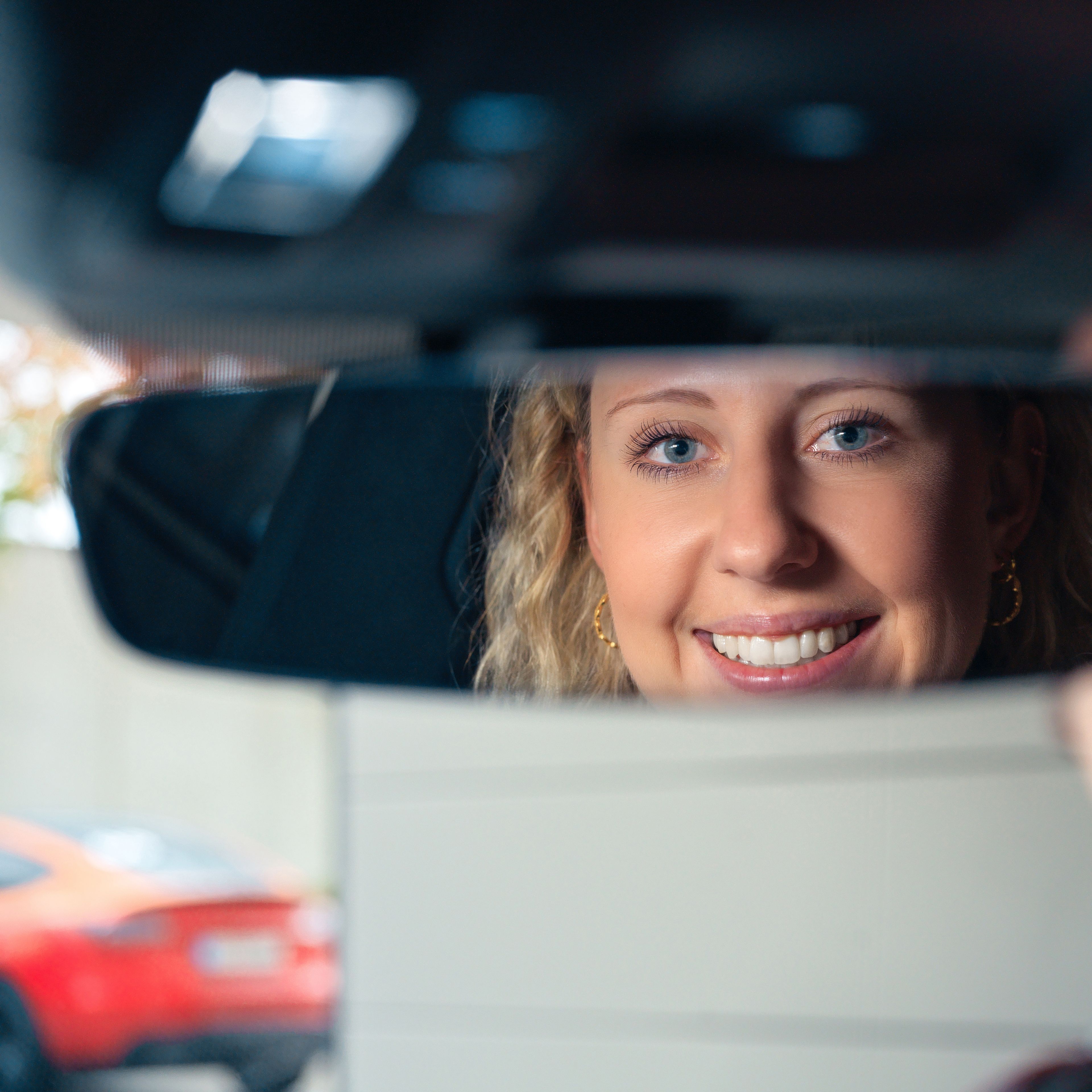 A lady adjusts a rearview mirror.