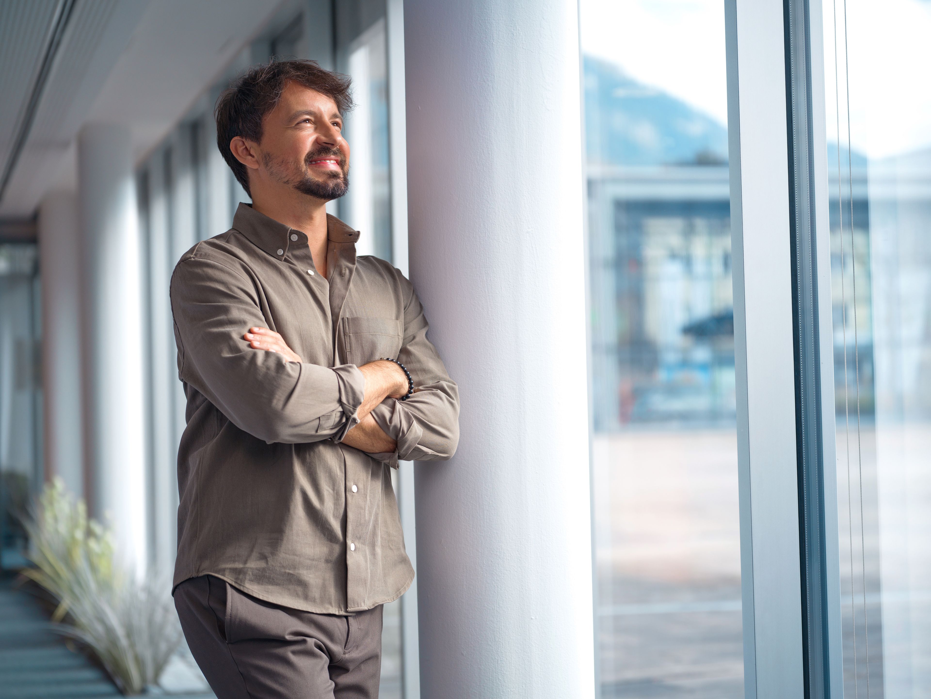 A man leans against a pillar in an office environment and smiles.