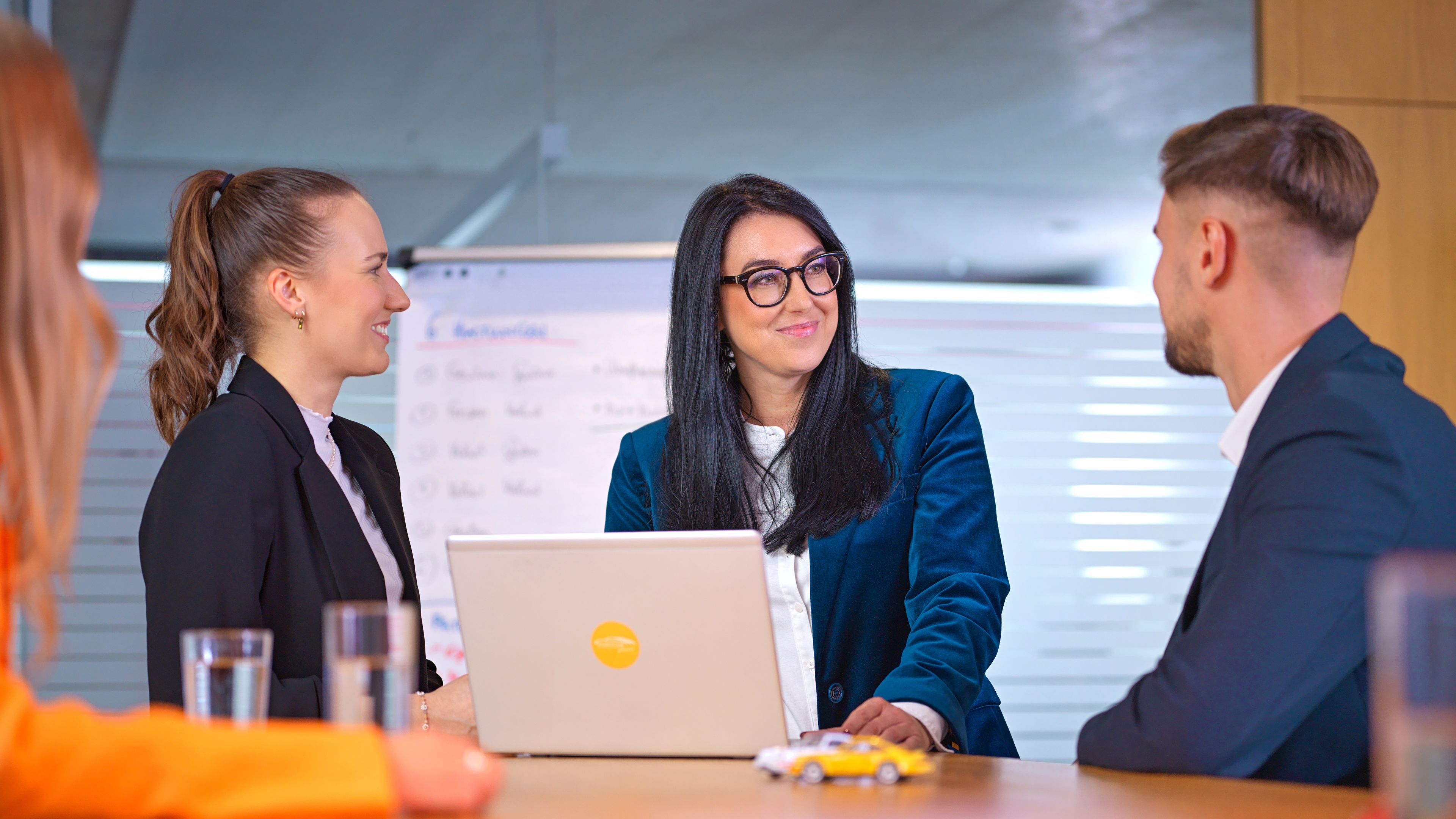 Hárman beszélgetnek egy laptop körül, előttük két modell autó.