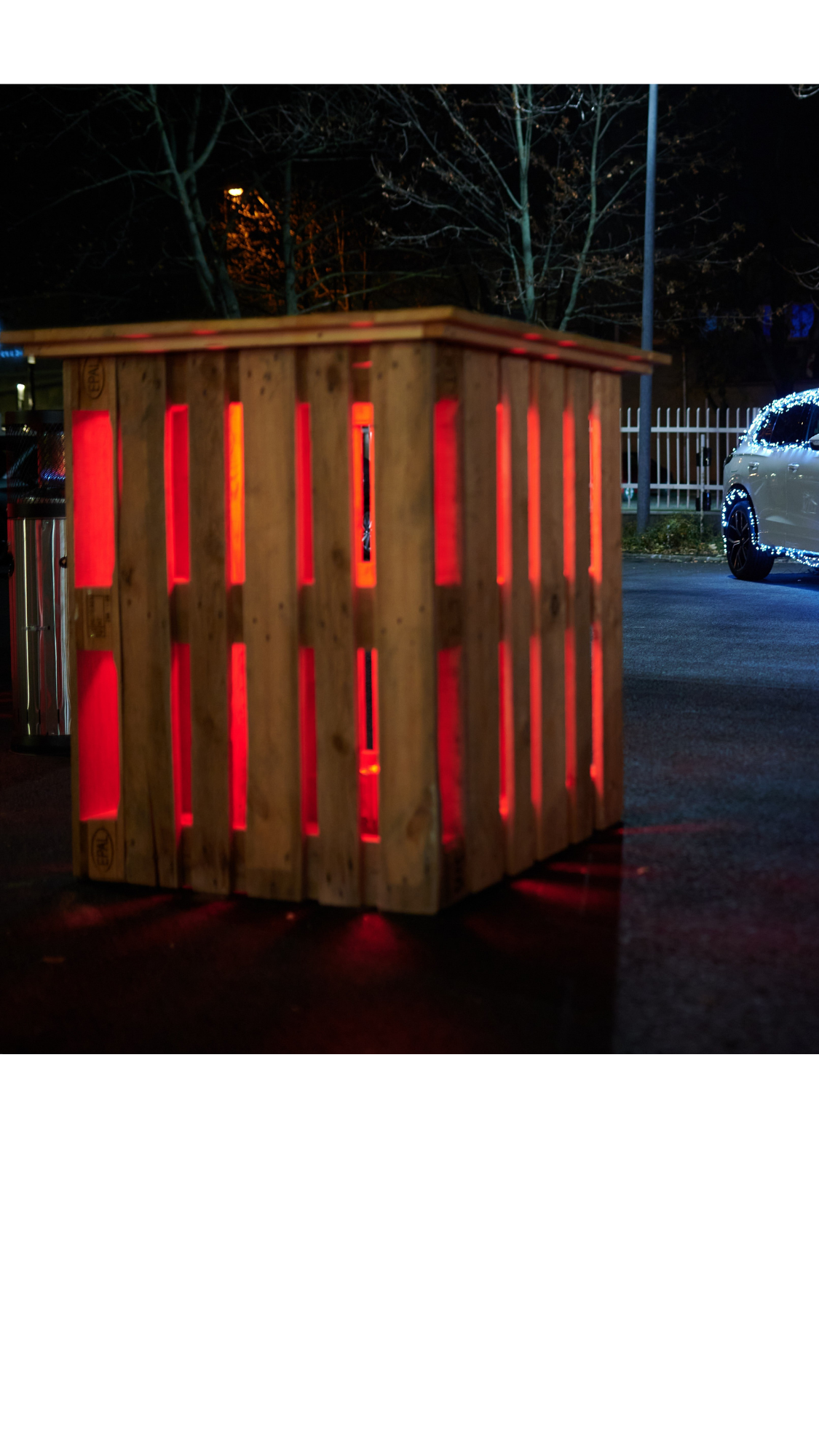 A car decorated with Christmas lights, an illuminated pallet table and a heater in front.