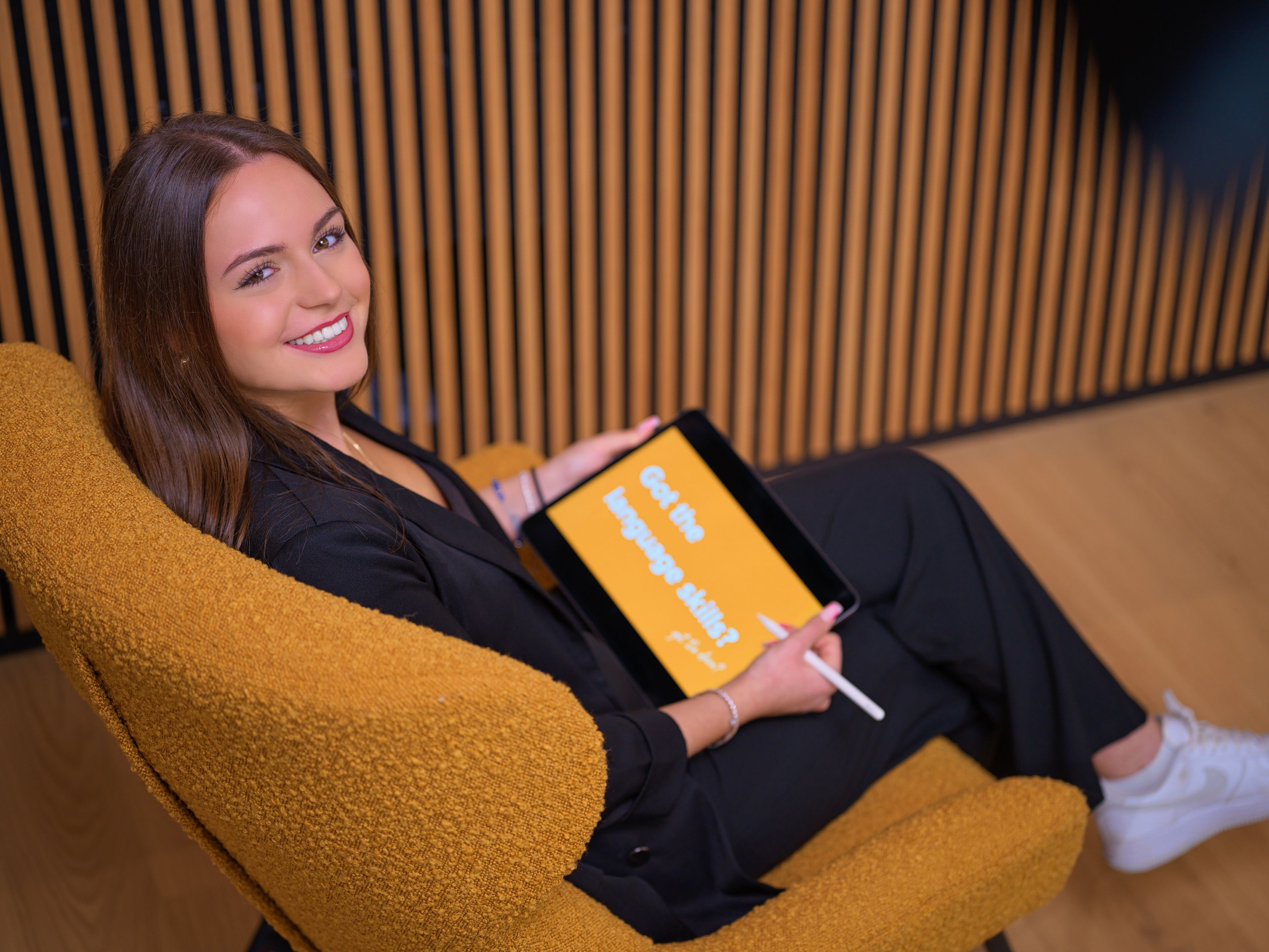 A young lady is sitting in an armchair with a tablet in her hand.