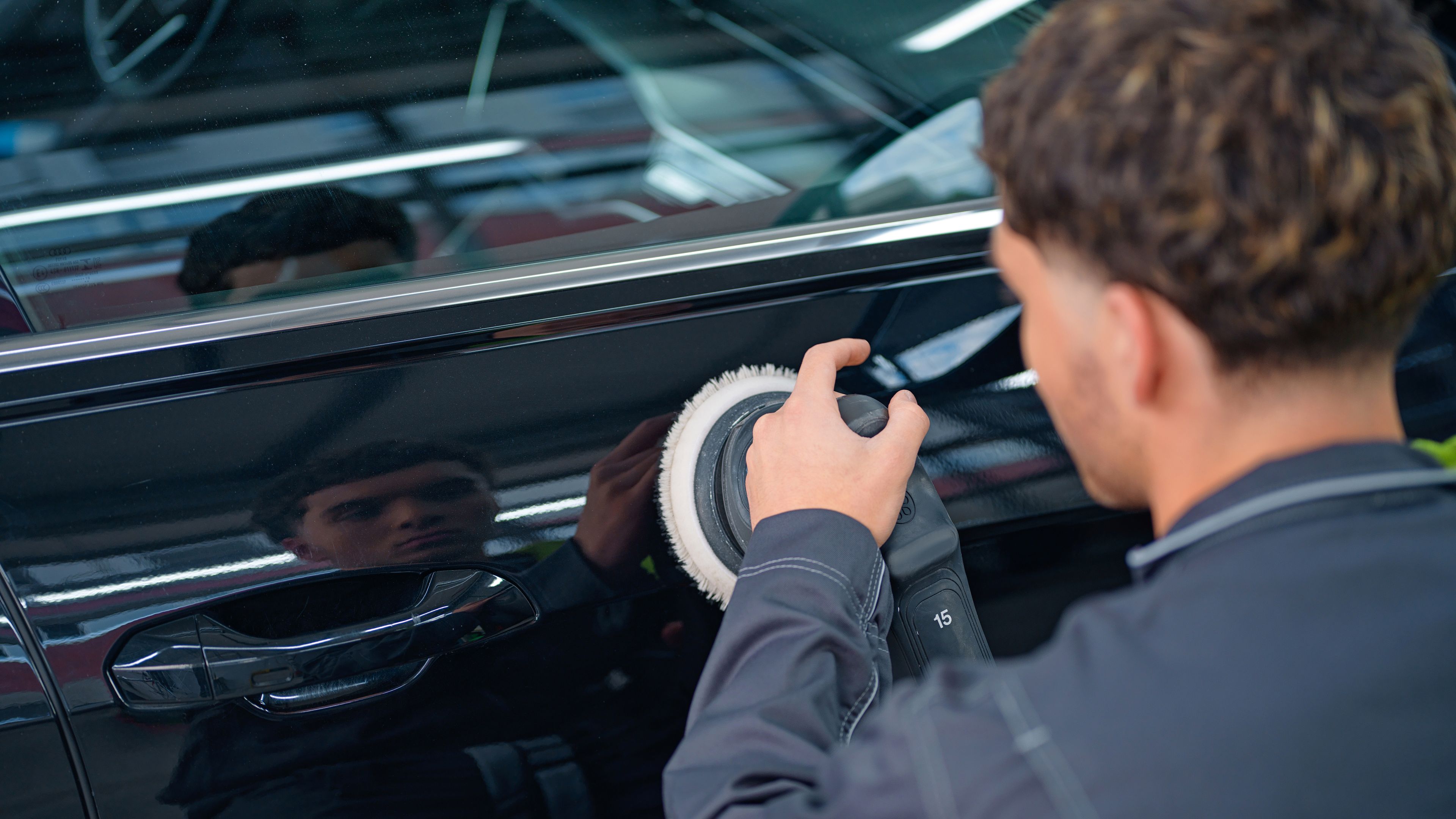 A black car is polished by a mechanic.