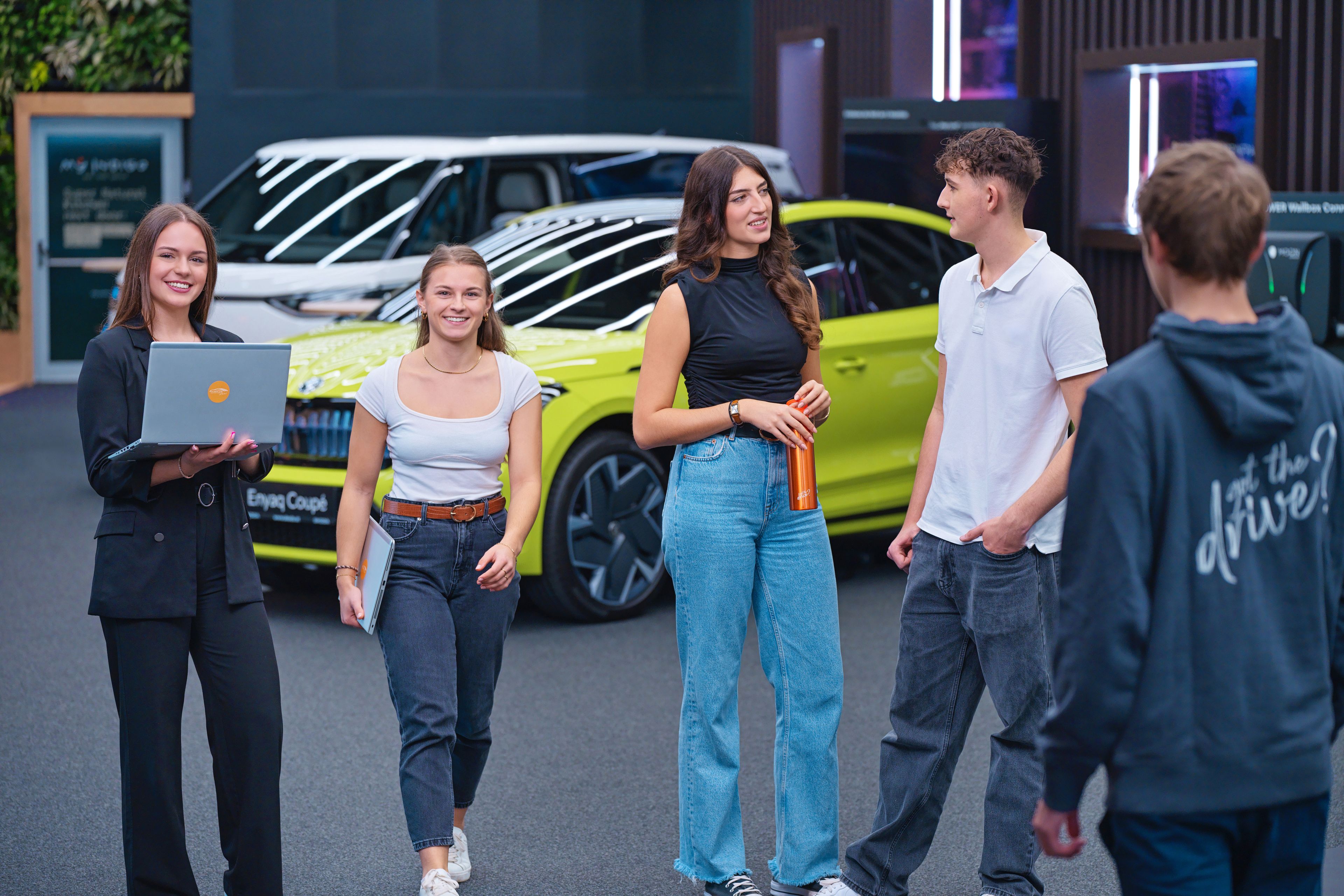 Young people talking, looking at laptops, behind them is a car showroom