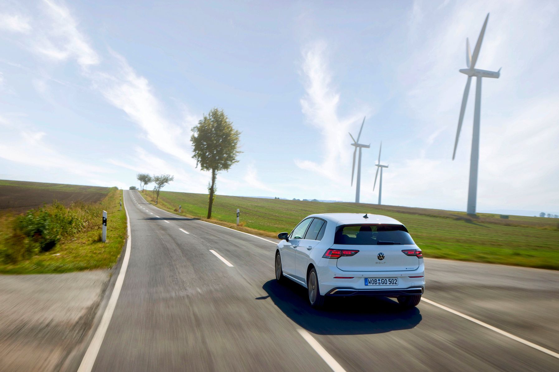 VW Golf vidéki úton, háttérben szélerőművek