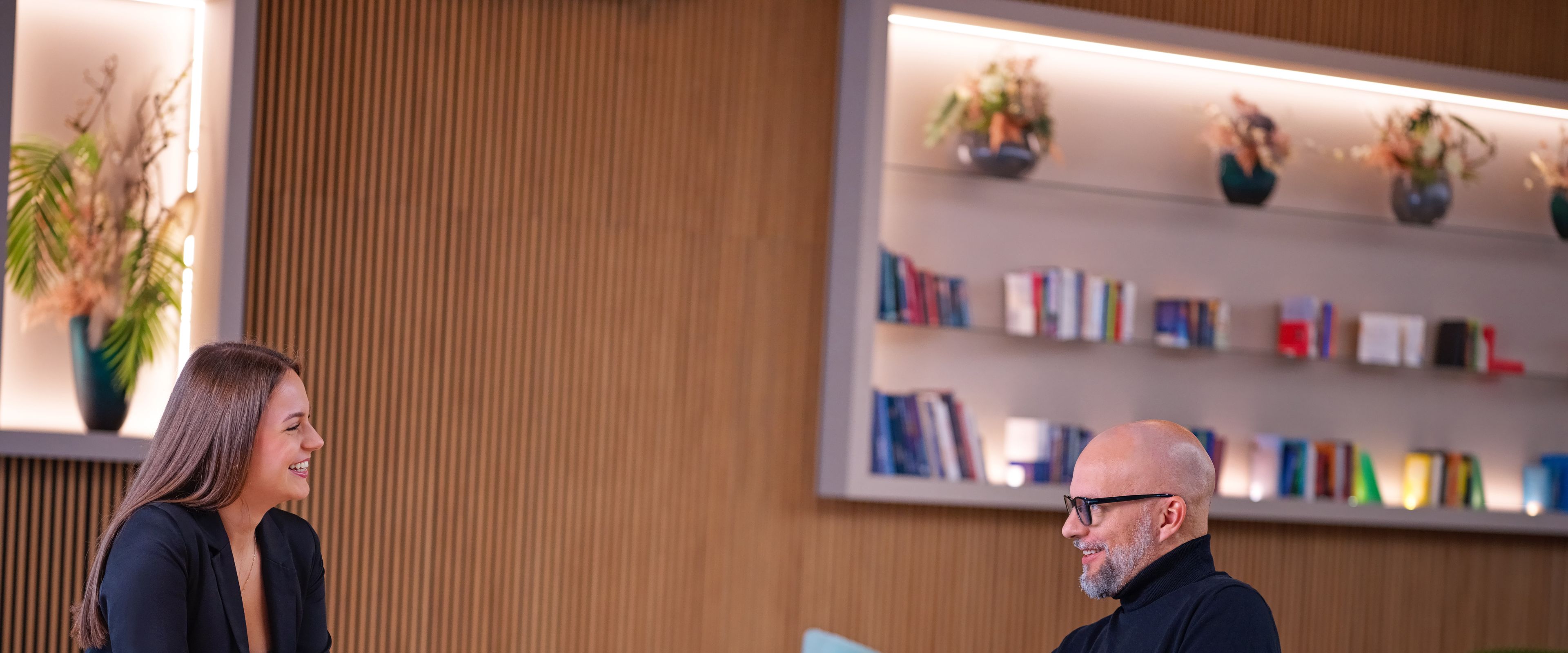 Ketten ülnek egy asztalnál, mögöttük könyvek, előttük kávé és víz.