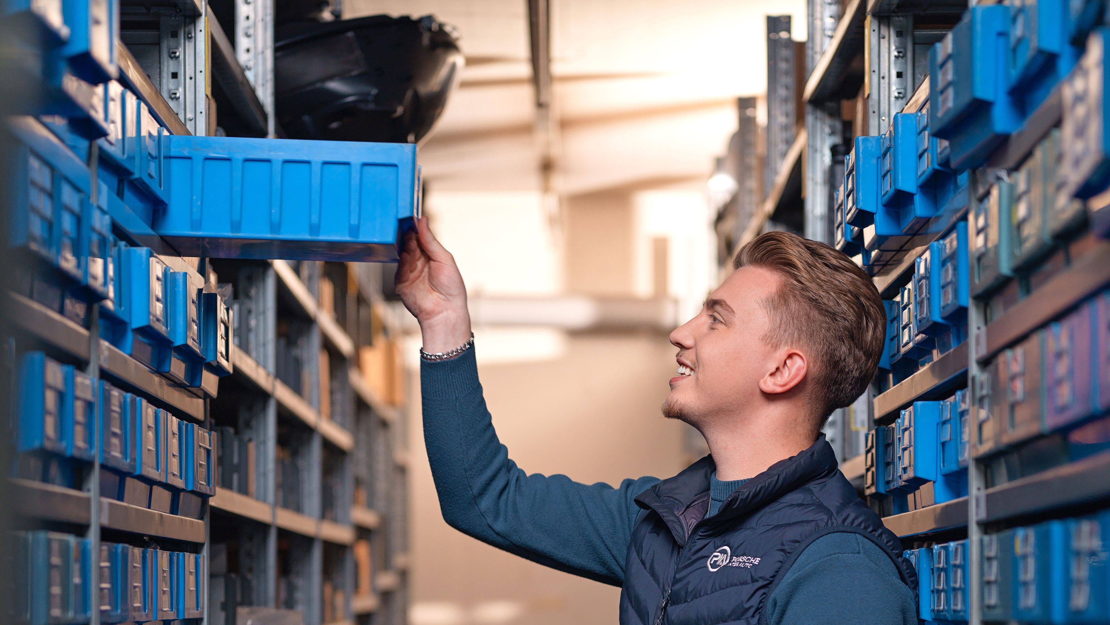 A young man pulls a blue box from a shelf in a warehouse.